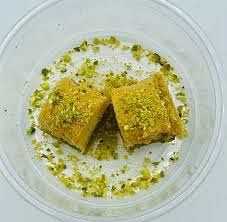 Baklava with pistachio topping cut in pieces in a clear to-go container