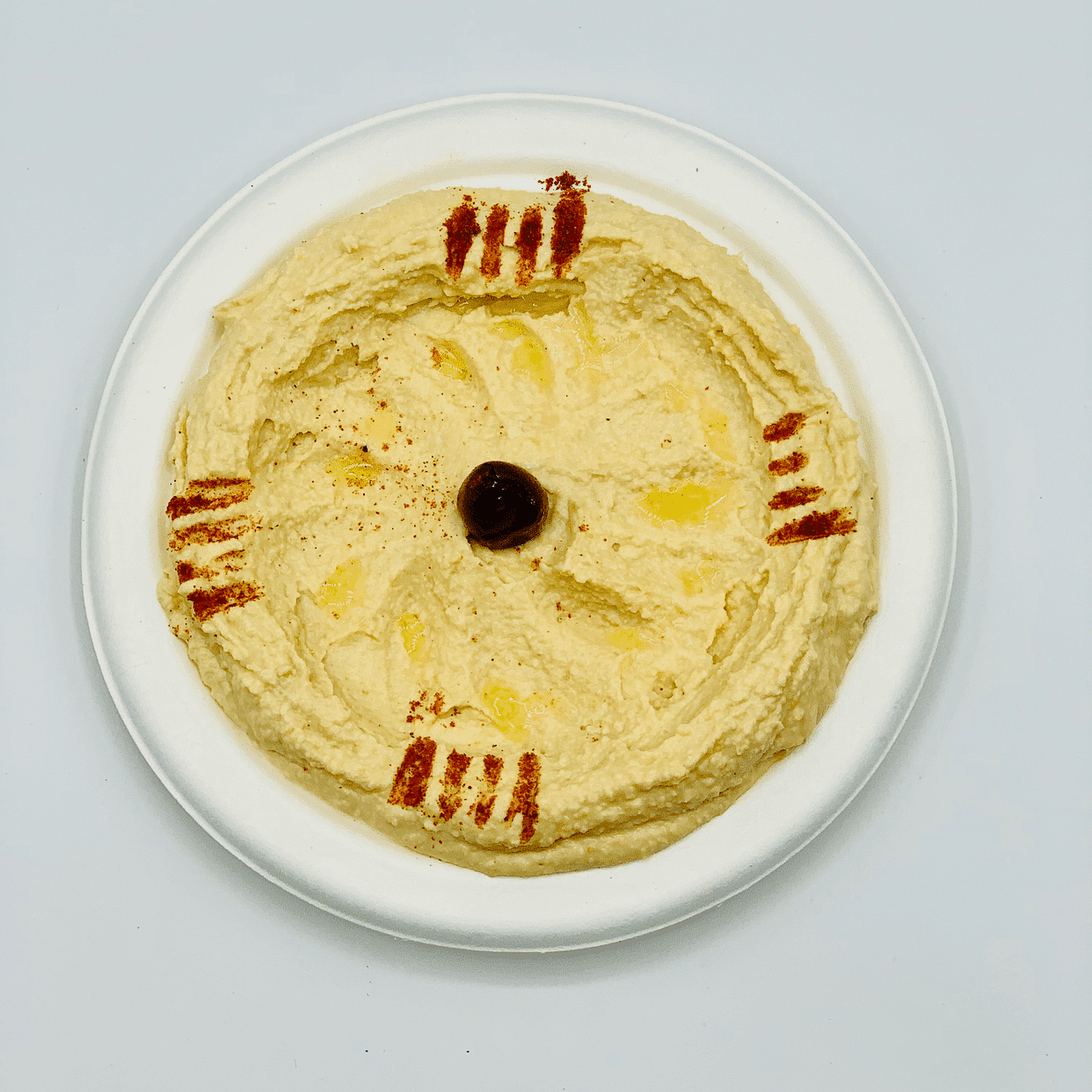 Plate of hummus with olive in the center and spice decoration